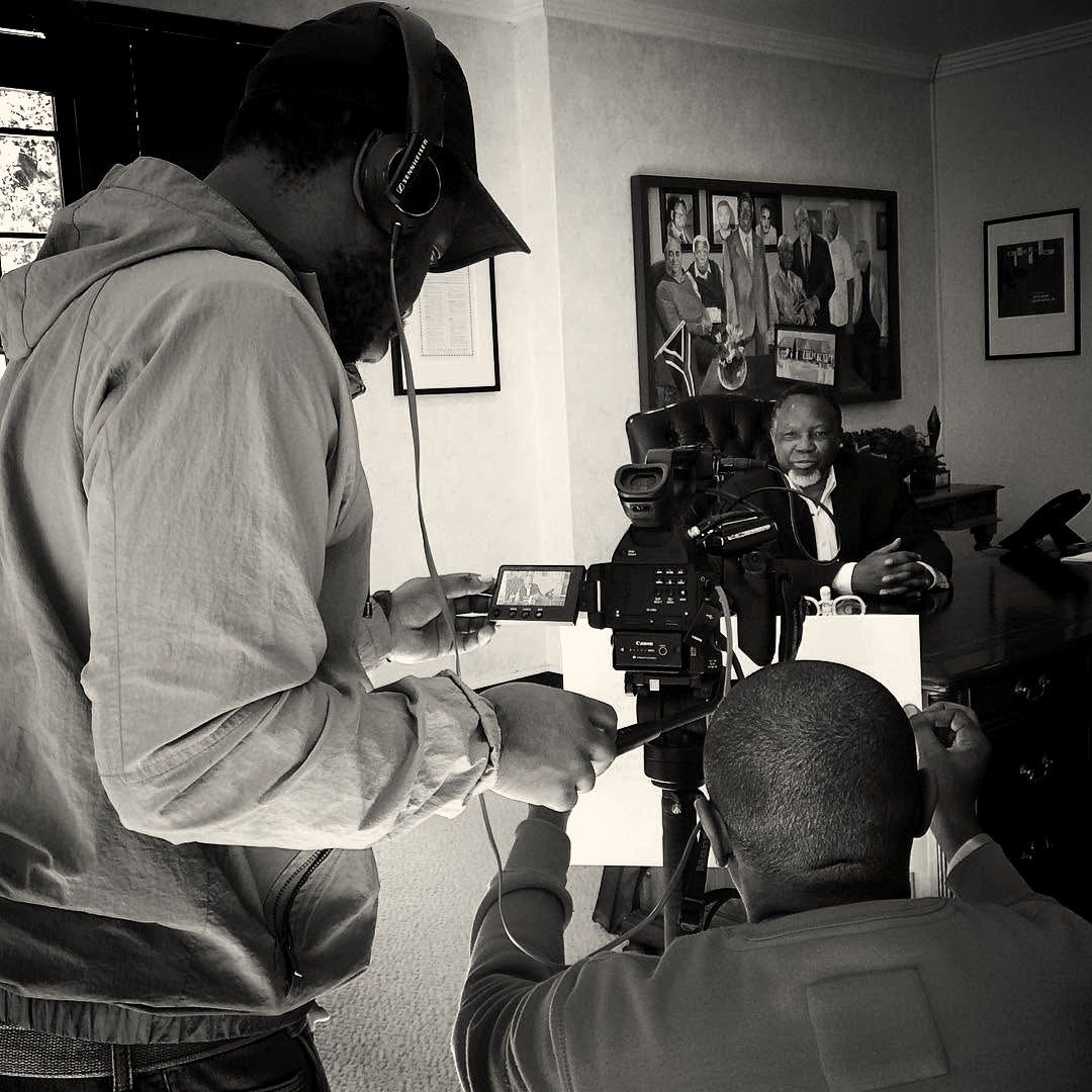 Two crew members filming a seated interview subject at a desk in an office