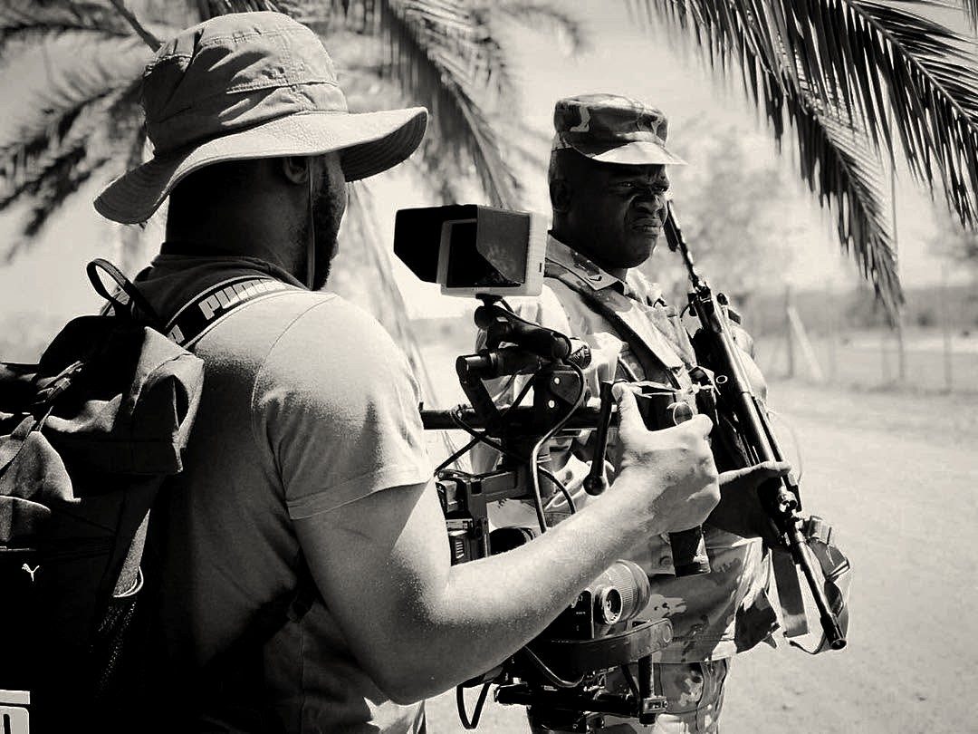 A camera operator with a gimbal rig filming a soldier on a dirt road