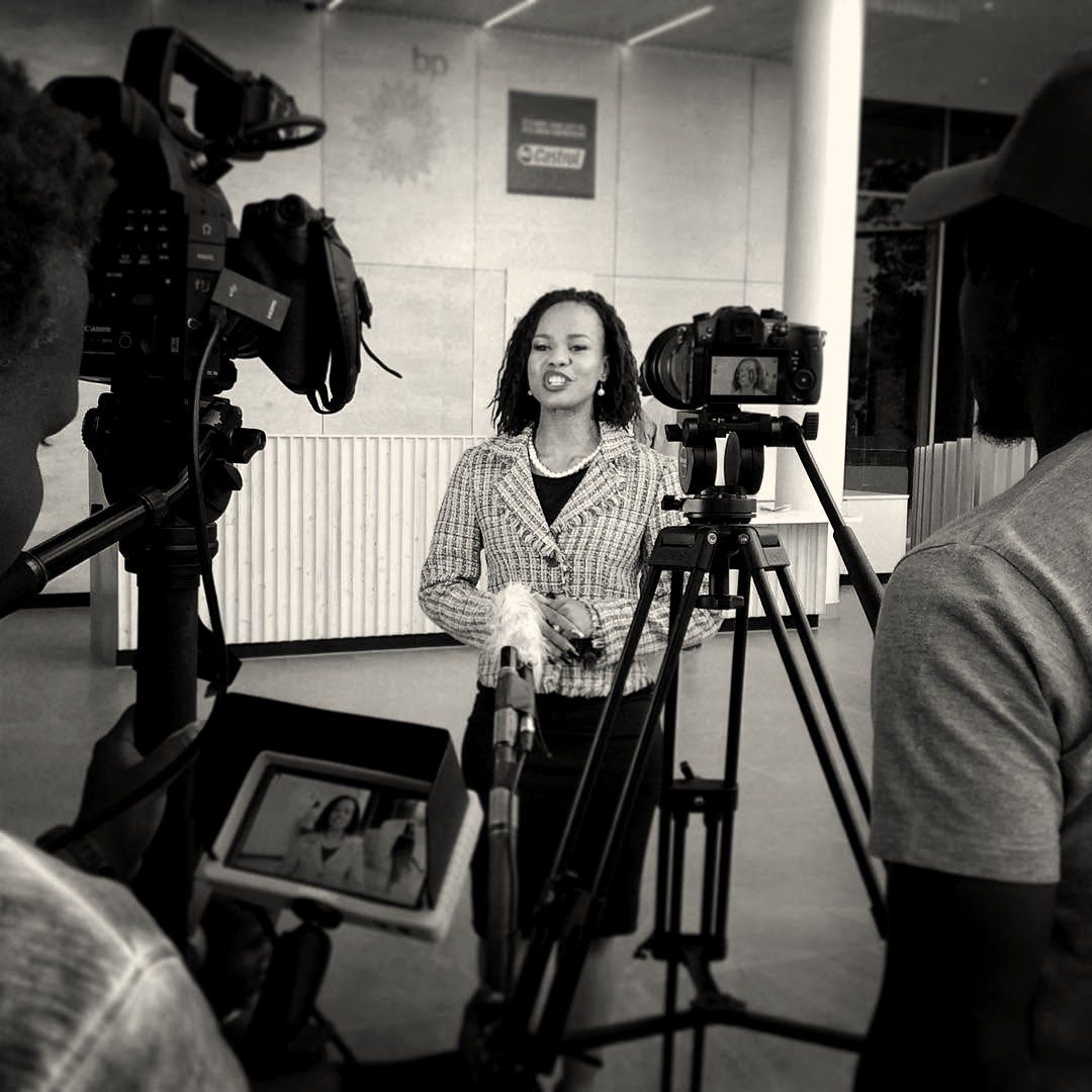 A presenter delivering a piece to camera in a corporate lobby, filmed by two cameras