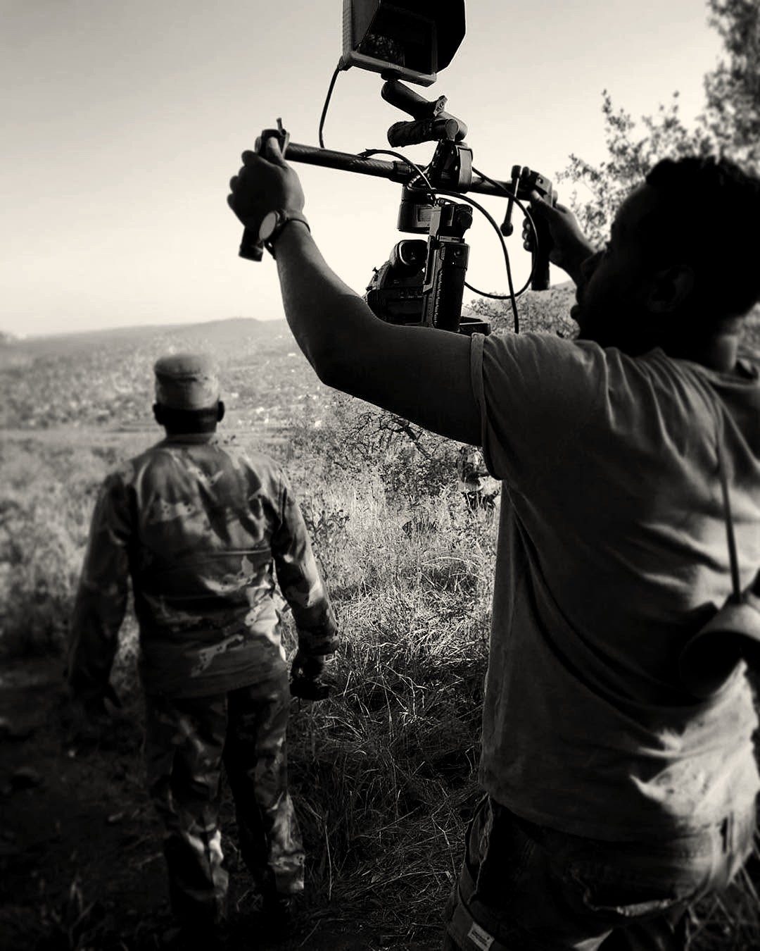 A camera operator holding a rig overhead to film a soldier looking out over a valley