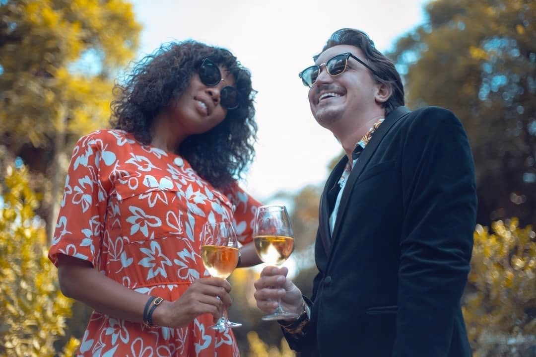 A woman and a man laughing with glasses of white wine in a garden