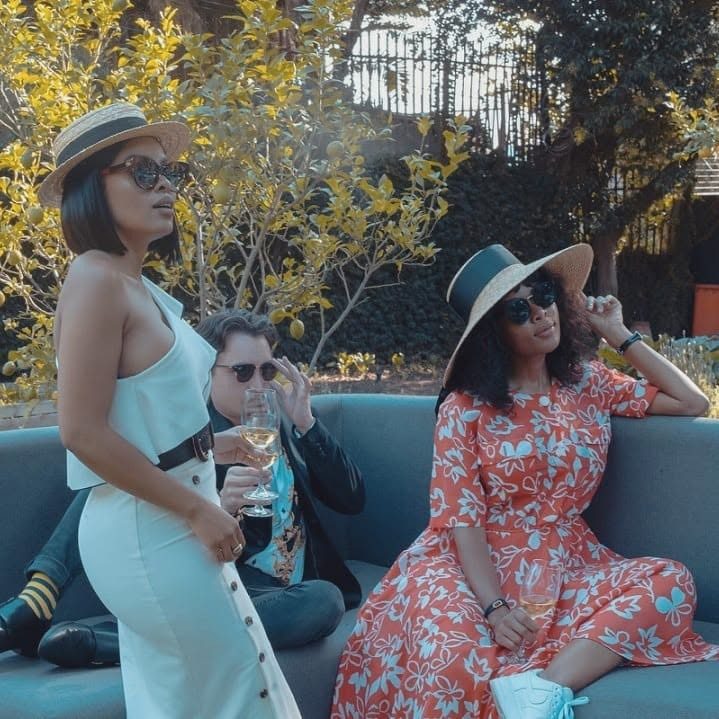 Three stylishly dressed people with wine glasses on an outdoor sofa