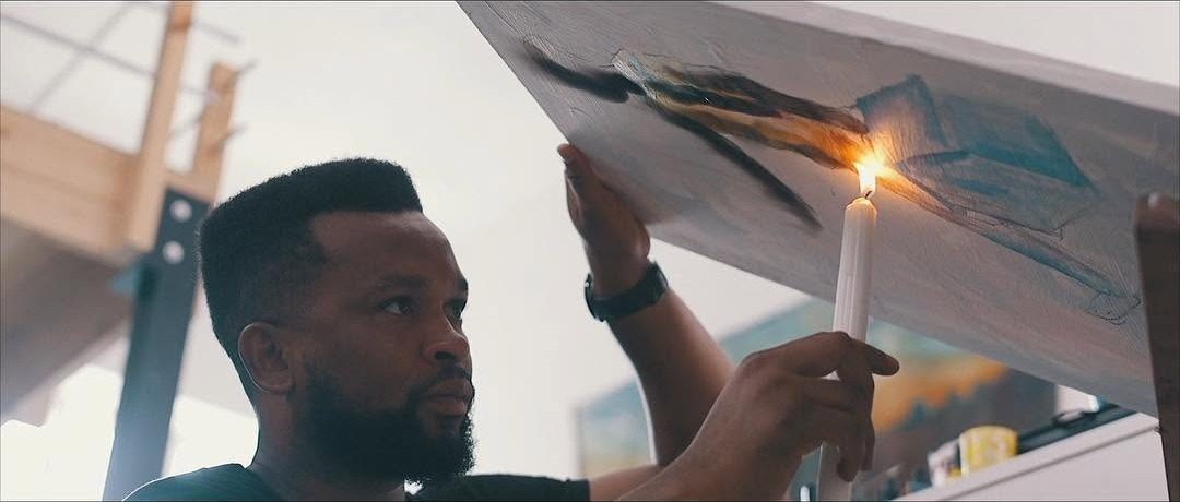 Film still: an artist holding a lit candle to a painted canvas